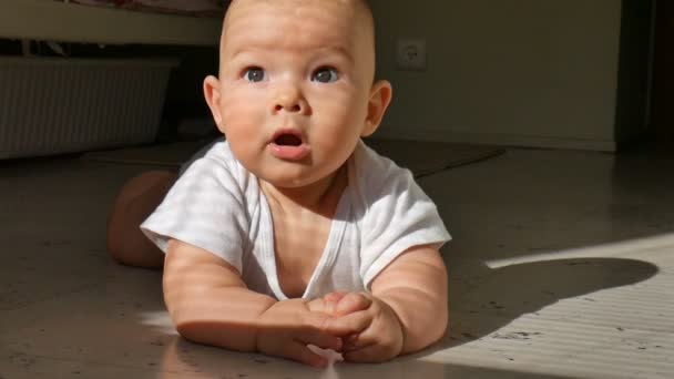Lindo bebé de seis meses está tirado en el suelo sonriendo alegremente. El niño golpea un arroyo en el suelo y se masturba vigorosamente las piernas
 - Imágenes, Vídeo