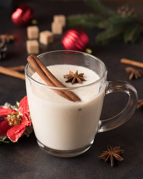 Traditional Christmas drink eggnog with cinnamon, anise stars and grated nutmeg in a glass mug on the metal tray table. Gingerbreads, eggs, and fir-tree decoration - Foto, immagini