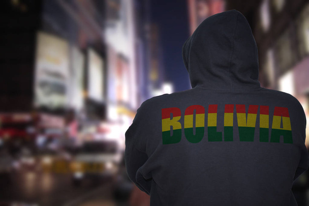 dangerous man standing on a city street at night with black hoodie with text bolivia on his back - Photo, Image