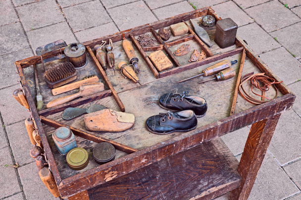 werktafel met kleine schoenen voor kinderen en oude instrumenten van de ambachtelijke schoenmaker voor reparatie en afwerking schoenen - Foto, afbeelding