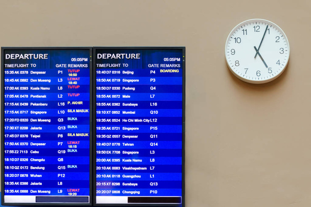 Tablica informacyjna lotniska, w pobliżu zegara z rąk, który pokazuje cztery minuty ostatnich pięciu, rozkład lotów. Malezja, Kuala Lumpur, Klia 2. - Zdjęcie, obraz
