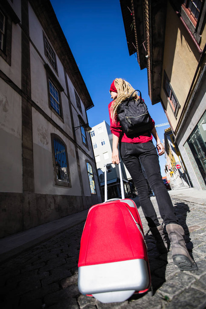 Hátsó nézet nő a járdán egy piros bőrönddel. Utazás és turizmus. - Fotó, kép