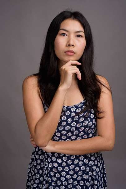 Жінка з Азії, одягнена в синю сукню на сірому фоні. - Фото, зображення