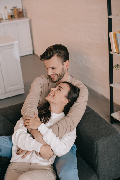 high angle view of smiling young couple embracing on couch at home - Photo, image