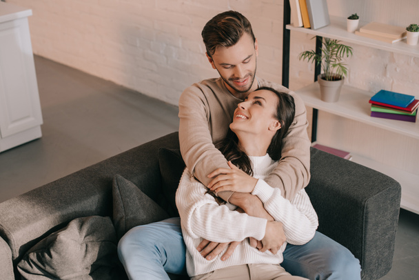 high angle view of happy young couple embracing on couch at home - Foto, afbeelding