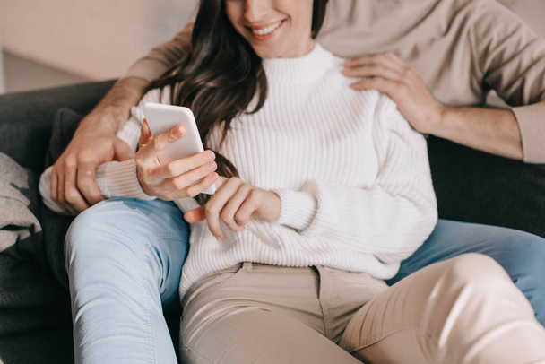 cropped shot of young couple using smartphone together on couch at home - Photo, Image