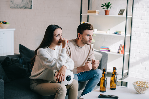 serious young couple watching football game on couch at home - Photo, Image