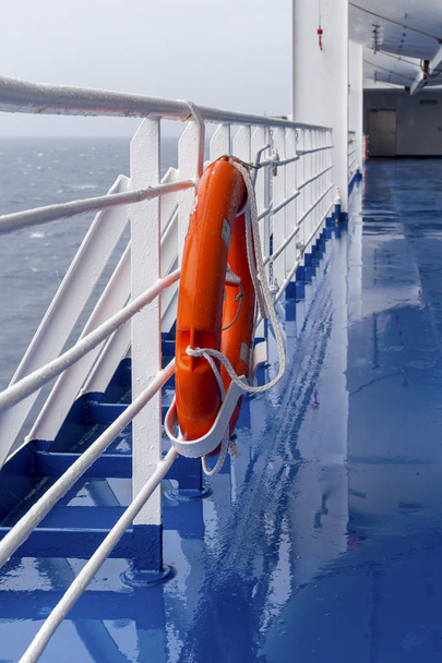 Bóia salva-vidas brilhante com luz pendurada no navio em um dia nublado contra o mar aberto
. - Foto, Imagem