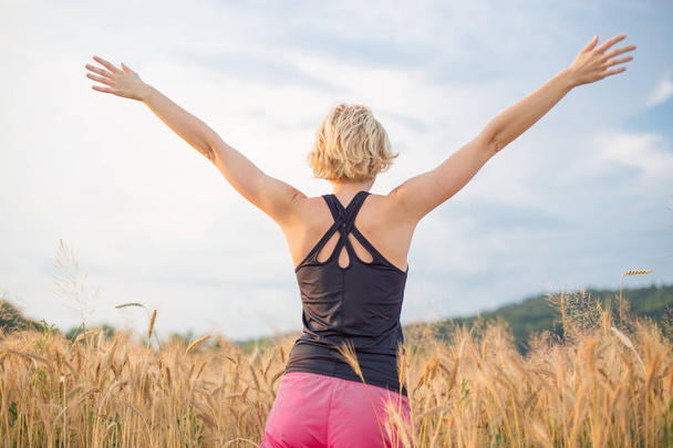 Femme sportive détendue, bras levés, profitant de la nature dans la belle matinée au champ de blé
. - Photo, image