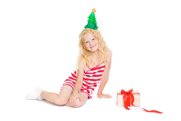 ünnepek, a tél és az ünnep fogalma-karácsonyi és újévi kártya aranyos szőke kislány piros és fehér farsangi jelmez ruha és a zöld fenyő fa kalap ajándék doboz elszigetelt fehér - Fotó, kép