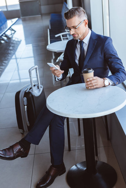 adult businessman using smartphone and drinking coffee at airport - Фото, изображение