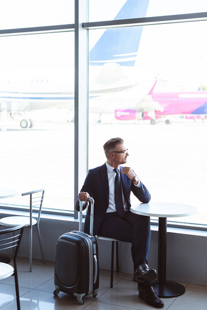 дорослий бізнесмен з дорожньою сумкою сидить за столом в аеропорту
 - Фото, зображення
