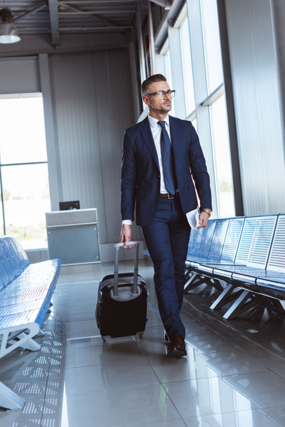 handsome businessman in glasses walking along departure lounge in airport - Photo, Image