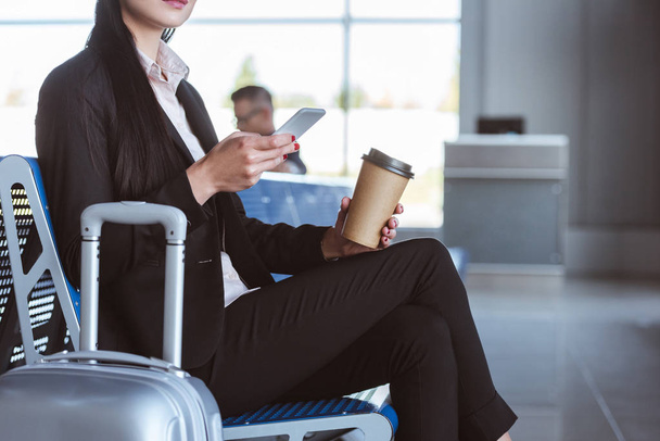 close up of young businesswoman with coffee to go using smartphone in departure lounge at airport - 写真・画像
