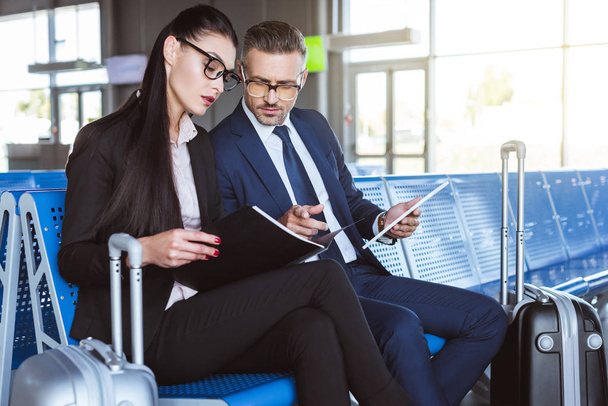empresário adulto usando tablet digital enquanto empresária segurando pasta preta no lounge de partida no aeroporto
  - Foto, Imagem