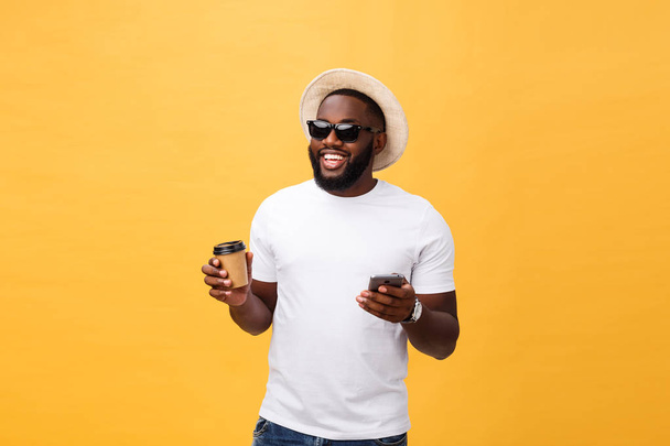 Όμορφος Αφρικανικός Αμερικανός με κινητό τηλέφωνο και πάρτε μακριά φλιτζάνι καφέ. Απομονωμένη πάνω από κίτρινο χρυσό φόντο. - Φωτογραφία, εικόνα