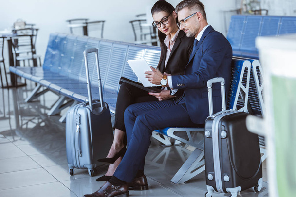 adult businessman and businesswoman sitting at departure lounge and using digital tablet in airport - Photo, Image