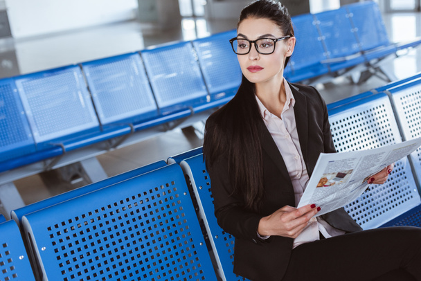 young beautiful businesswoman in glasses reading newspaper at departure lounge in airport - 写真・画像
