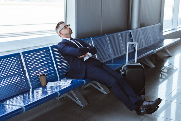 exhausted businessman in glasses sitting near window at departure lounge  - 写真・画像