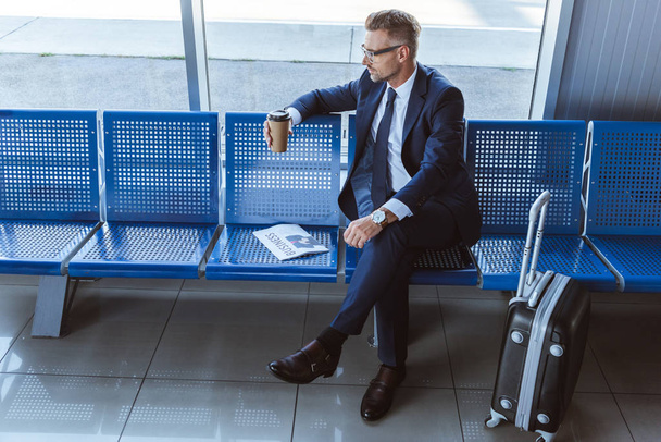 Geschäftsmann in Brille sitzt am Fenster mit Zeitung und Coffee to go im Flughafen - Foto, Bild
