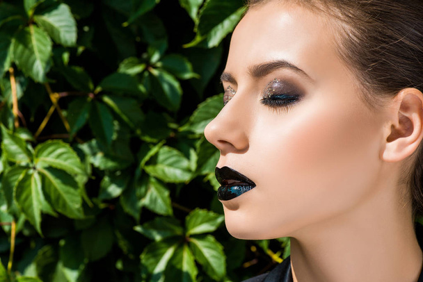 young beautiful woman with glittery makeup and closed eyes at green leaves background  - 写真・画像