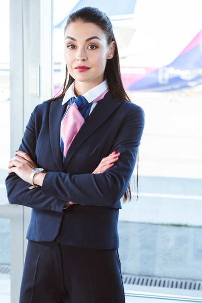 adulto feminino aeroporto trabalhador de pé com braços cruzados perto da janela
  - Foto, Imagem