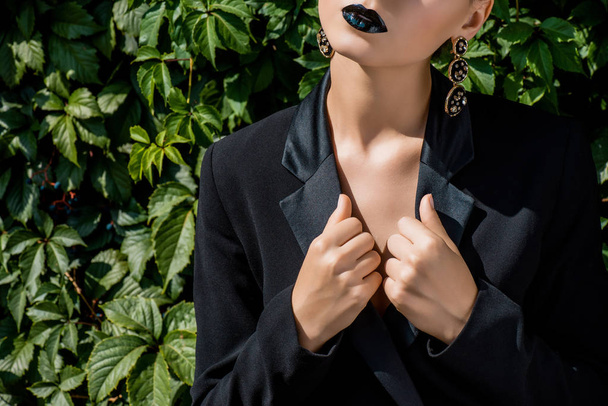 young woman with closed eyes holding black jacket on green background - Foto, afbeelding