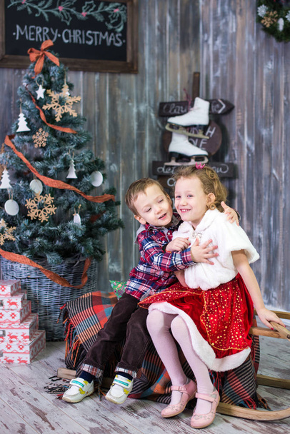 A háttérben a karácsonyi ajándékok és két kis gyermek, testvér és nővér, ül. Kellemes karácsonyi ünnepeket és boldog ünnepek! Karácsonyi fa beltéri. - Fotó, kép