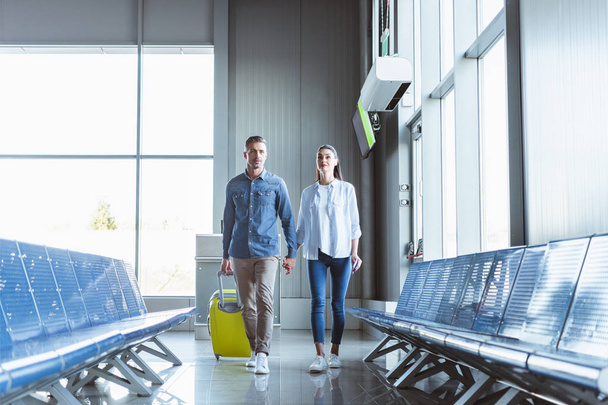 Romantic couple holding hands walking with yellow baggage in the airport - Fotó, kép