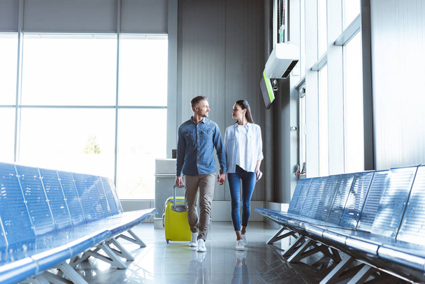 Mies ja nainen kävelemässä keltainen matkalaukku lentokentällä
 - Valokuva, kuva