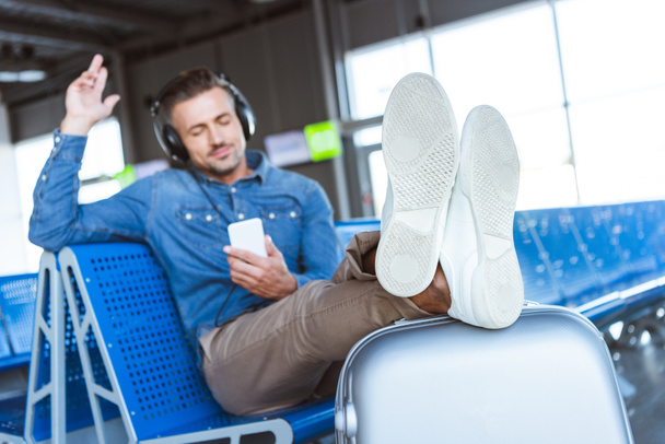 Человек наслаждается музыкой и расслабляется в ожидании своего рейса в аэропорту
 - Фото, изображение