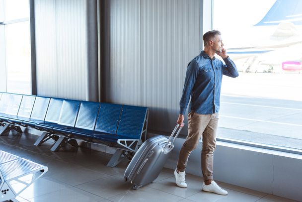 Jóképű férfi Ezüst csomagokkal, beszél a telefonon, és a gyaloglás a repülőtéren - Fotó, kép