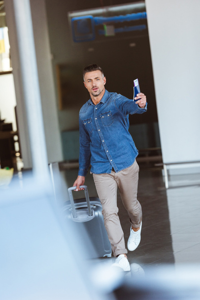 Ο άνθρωπος με τα πόδια στο αεροδρόμιο και δείχνοντας κάτι με το διαβατήριο στο χέρι του - Φωτογραφία, εικόνα