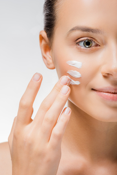 young beautiful woman applying white cream with fingers on cheek - 写真・画像