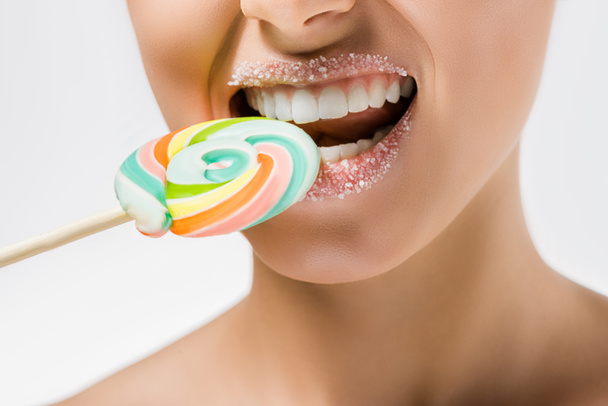 Nahaufnahme einer jungen Frau mit Zucker auf den Lippen, die farbigen Lutscher beißt - Foto, Bild