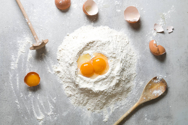 Proces van bakken, bloem en eieren op een grijze tafel. Van bovenaf bekijken. - Foto, afbeelding
