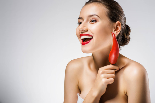 young smiling beautiful woman with red lips holding chili pepper near face - Foto, Bild