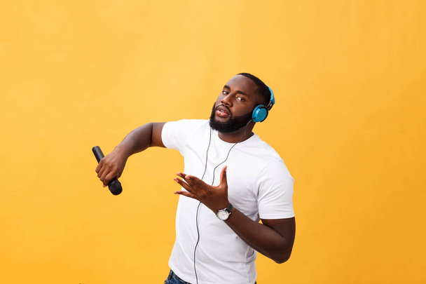 Portrait de joyeux chic chic beau Africain tenant le microphone et ayant des écouteurs sur la tête écouter de la musique chanson de chant profiter des vacances de week-end isolé sur fond jaune
 - Photo, image