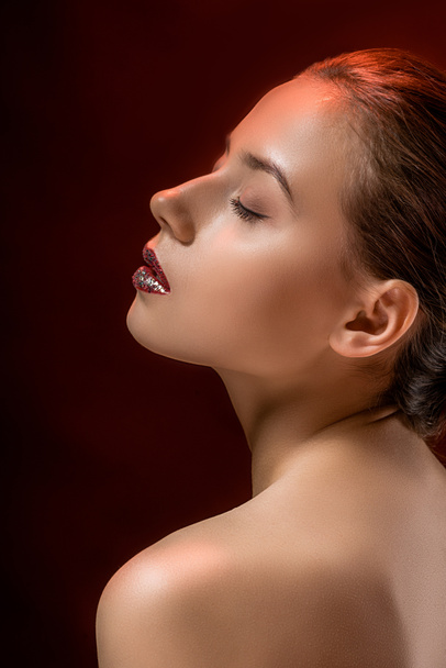 young woman with glittery lips and closed eyes on burgundy background - Photo, Image