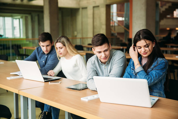 Ομάδα από φοιτητές που σπουδάζουν στη βιβλιοθήκη του σχολείου, ένα κορίτσι και ένα αγόρι είναι χρησιμοποιώντας ένα φορητό υπολογιστή και σύνδεση στο internet - Φωτογραφία, εικόνα