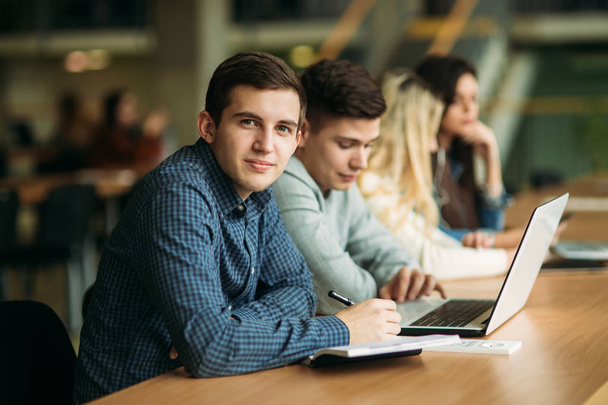 Eine Gruppe von College-Studenten, die in der Schulbibliothek lernen, ein Mädchen und ein Junge benutzen einen Laptop und verbinden sich mit dem Internet. Junge schaut in die Kamera - Foto, Bild