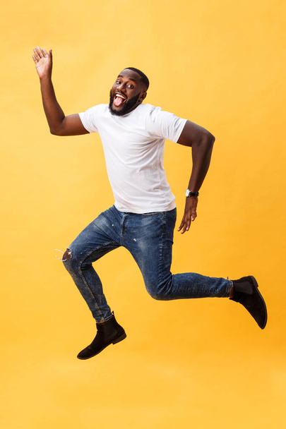 Full length of handsome young black man jumping against yellow background. - Zdjęcie, obraz