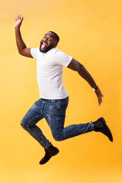 Full length of handsome young black man jumping against yellow background. - Photo, Image