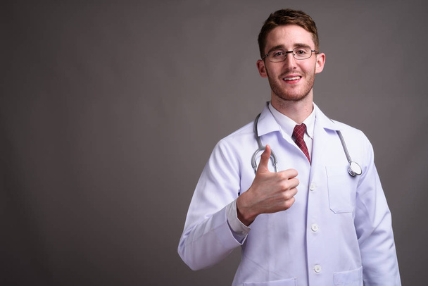 Όμορφος νεαρός γιατρός φοράει γυαλιά εναντίον γκρι έκφραση - Φωτογραφία, εικόνα