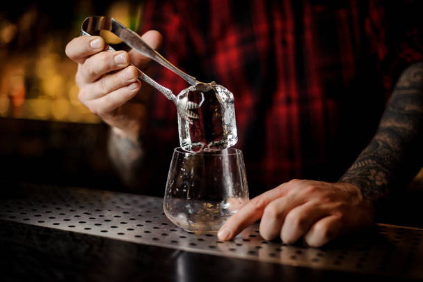 Barkeeper Hand legt einen großen Eiswürfel in eine Whiskey-Dose auf der Theke - Foto, Bild
