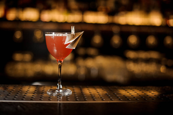 Decorated glass filled with fresh Paper Plane cocktail on the bar counter on the background of lights - 写真・画像