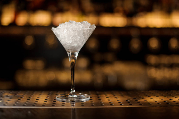 Elegant martini glass filled with ice on the bar counter against the golden lights of bar - Fotografie, Obrázek
