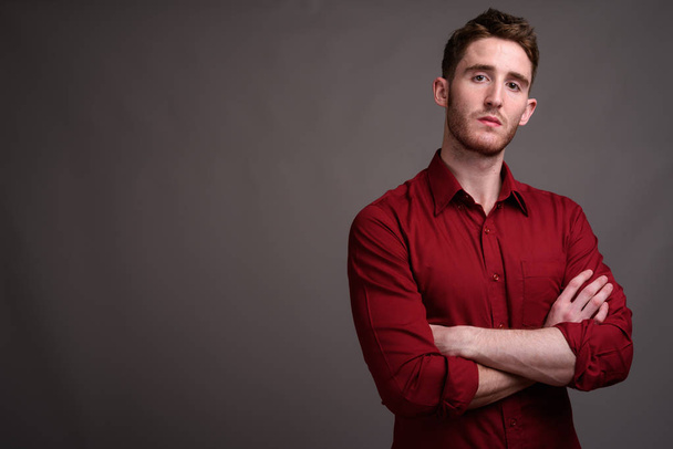 Mladý pohledný podnikatel na sobě červené tričko proti šedé pozadí - Fotografie, Obrázek