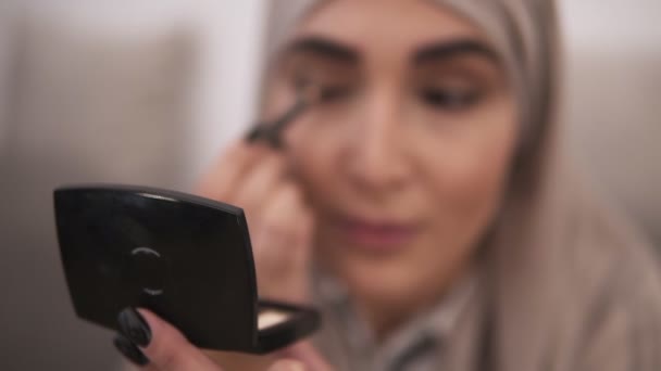 Muslim woman doing contour on her eye using black eyepencil. Modern life of muslim people. Front view of a woman in beige hijab - Video, Çekim