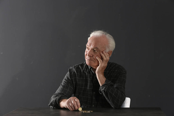 Poor elderly man with coins sitting at table on dark background - Фото, зображення
